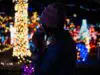 A person sipping coffee in front of holiday lights.